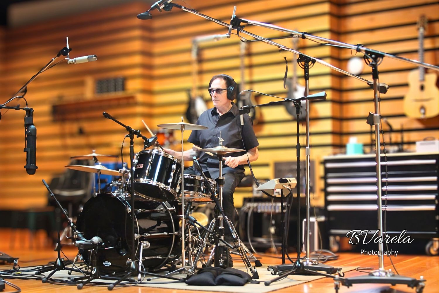 Musician playing drums in a professional recording studio with microphones and acoustic panels in the background.