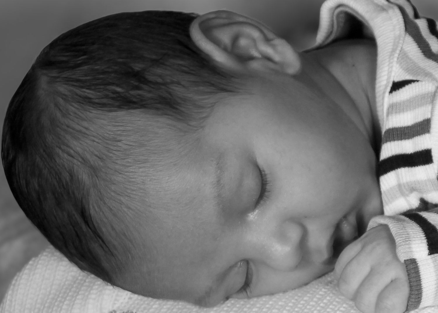 Black and white close-up photo of a sleeping newborn baby with delicate features and striped clothing.