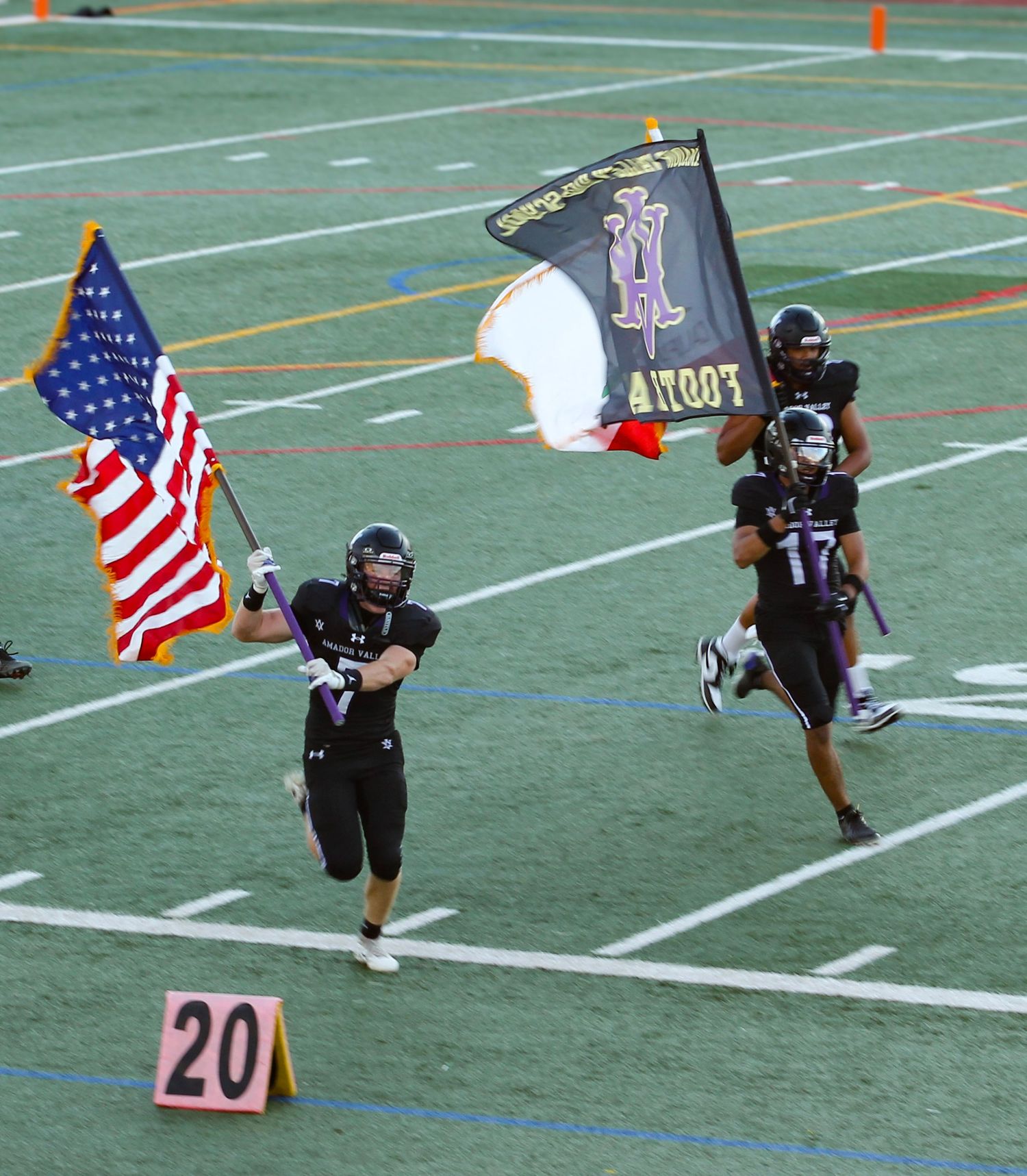 Football players running onto field carrying American flag and team banner with number 17 jersey visible.