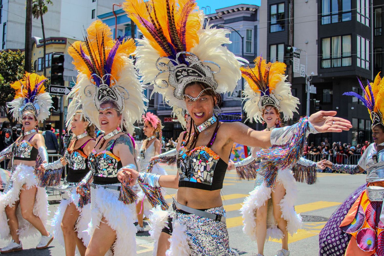 Colorful carnival dancers in elaborate feathered headdresses and sequined costumes perform in a vibrant street parade.