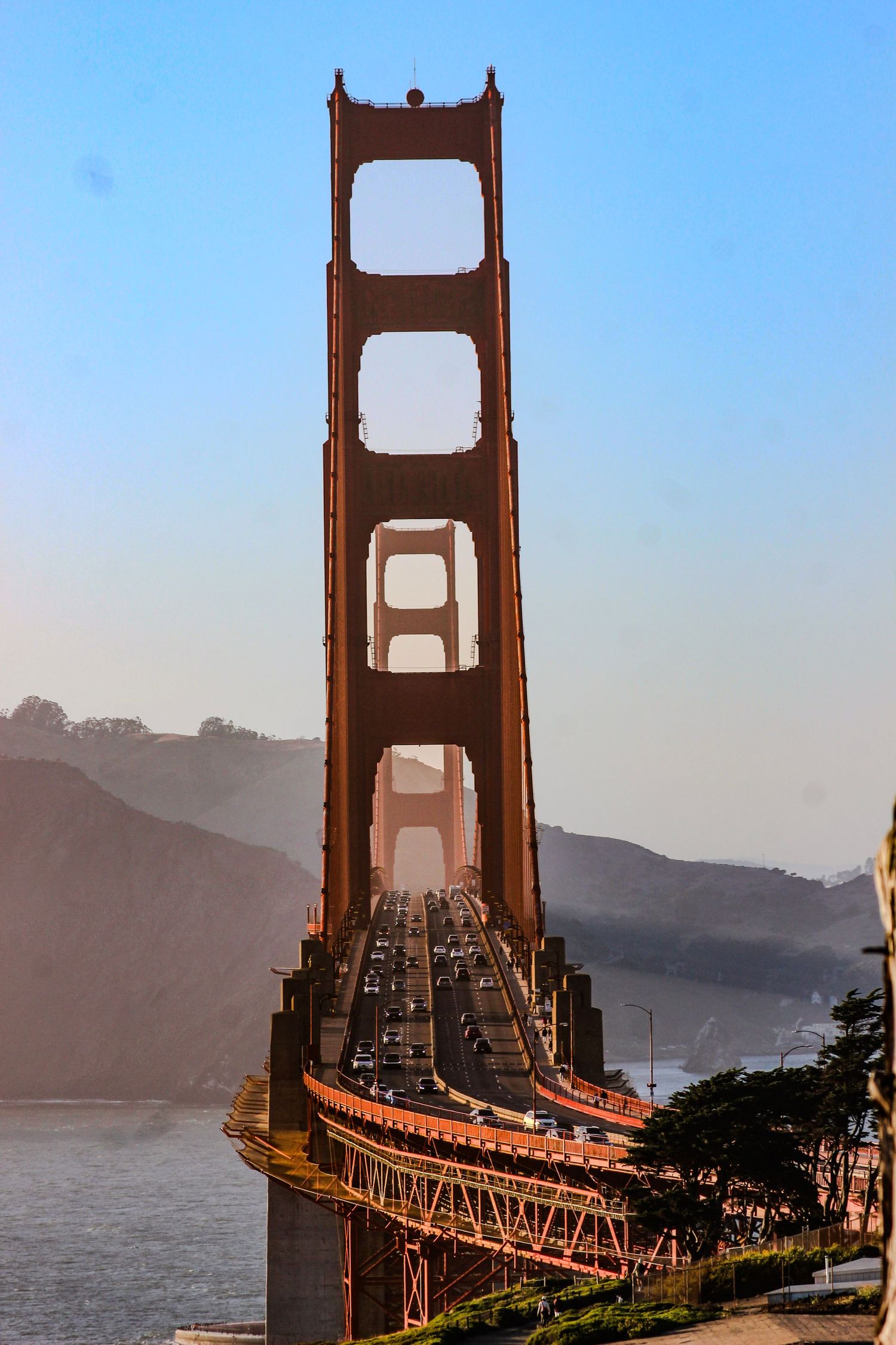 Golden Gate Bridge tower with traffic on the roadway, spanning San Francisco Bay with misty hills in the background.