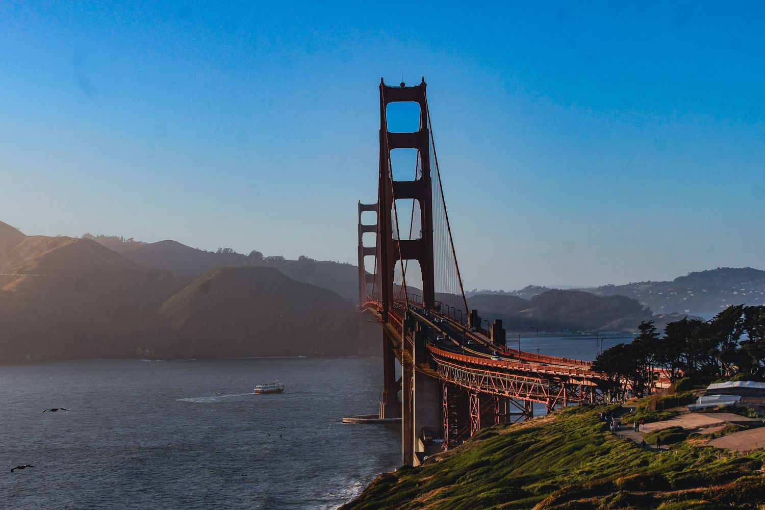 Golden Gate Bridge at sunset with misty hills, blue sky, and San Francisco Bay in the background.