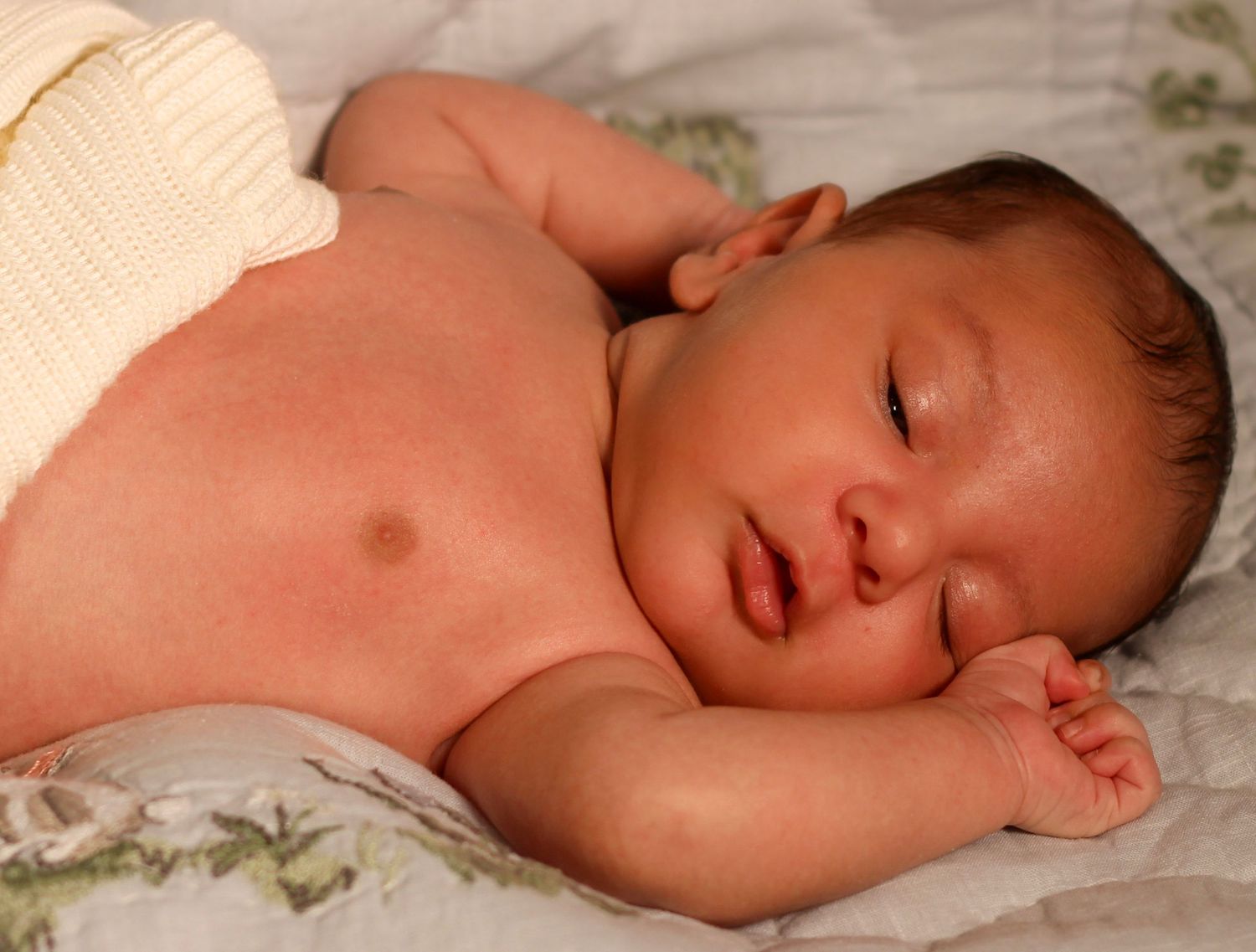 Peaceful newborn baby sleeping on a soft floral blanket, with tiny hands tucked under cheek.