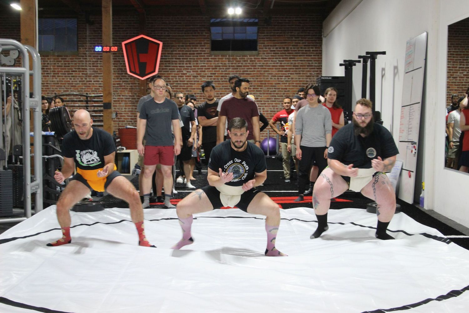 Athletes compete in sumo wrestling matches at an indoor gym with spectators watching in the background.