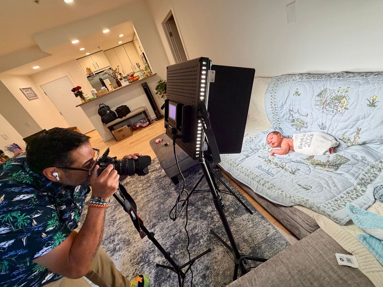 Photographer capturing newborn baby photos with professional lighting setup in a cozy living room setting.