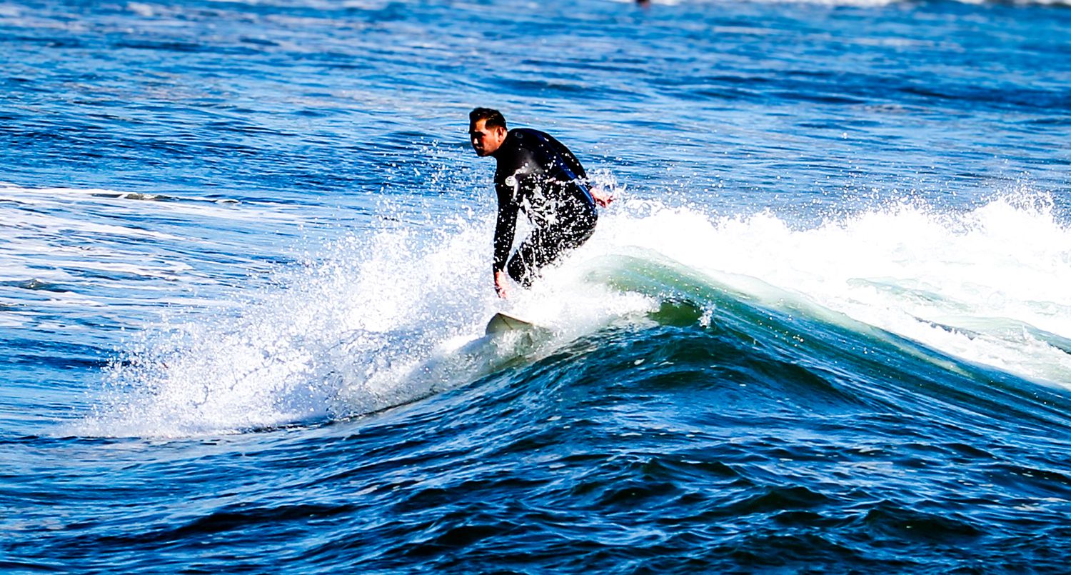 A surfer in a black wetsuit skillfully rides a blue ocean wave on a sunny day.