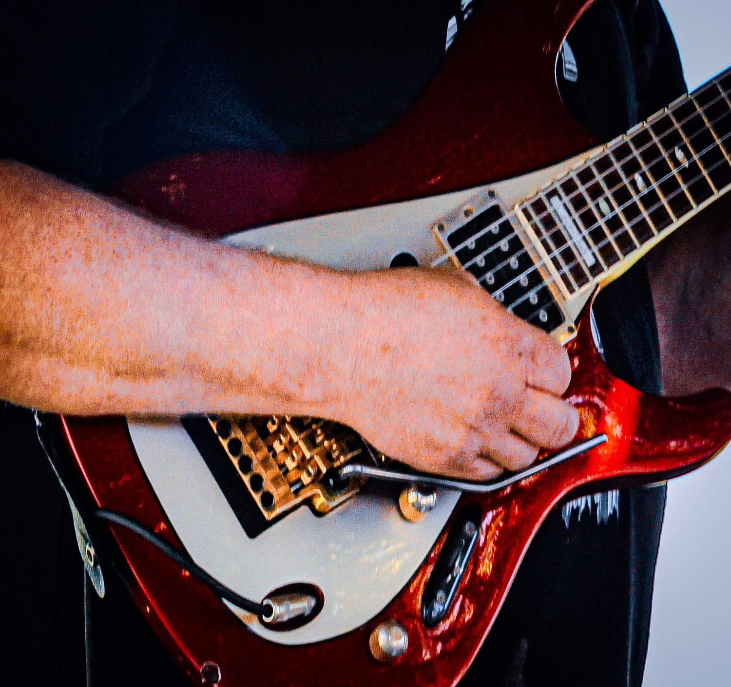 Close-up of a musician strumming a red and white electric guitar with both hands during a live performance.