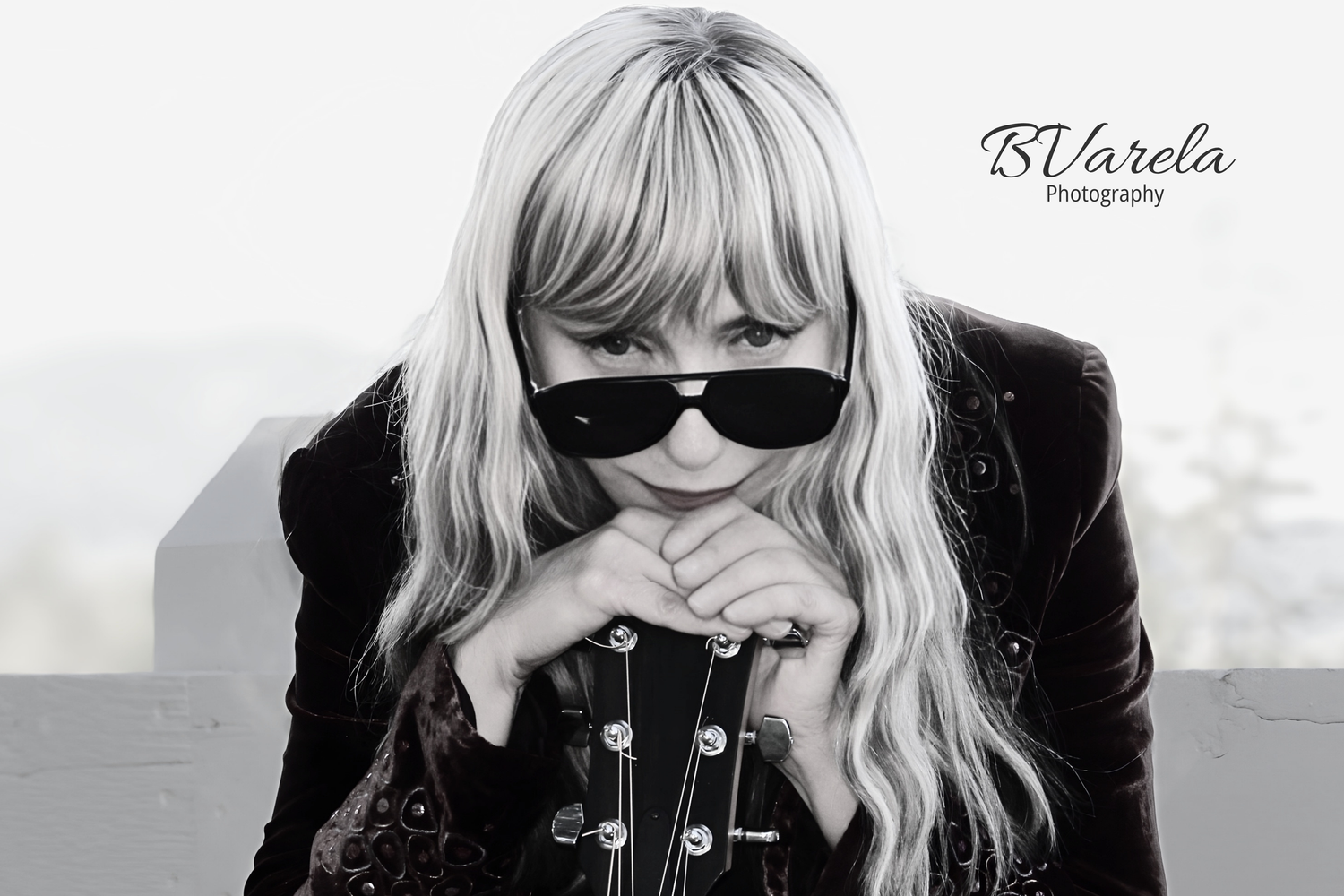 Black and white portrait of a blonde woman in sunglasses and dark jacket, leaning forward, BVarela Photography.