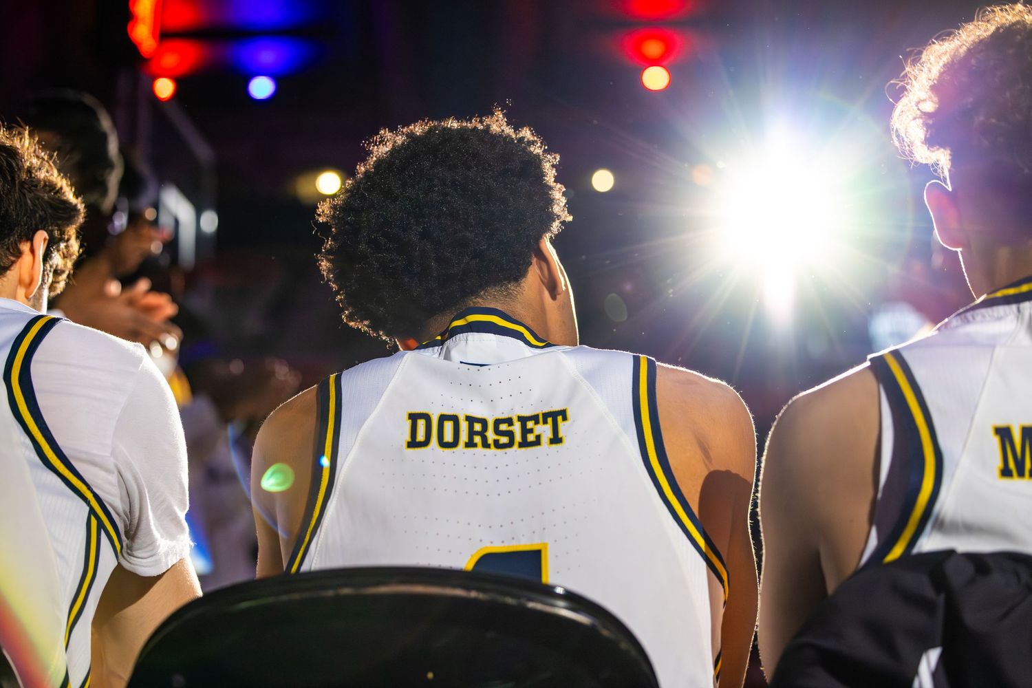 Basketball player wearing a Dorset jersey sits on the bench under colorful lights during a game.
