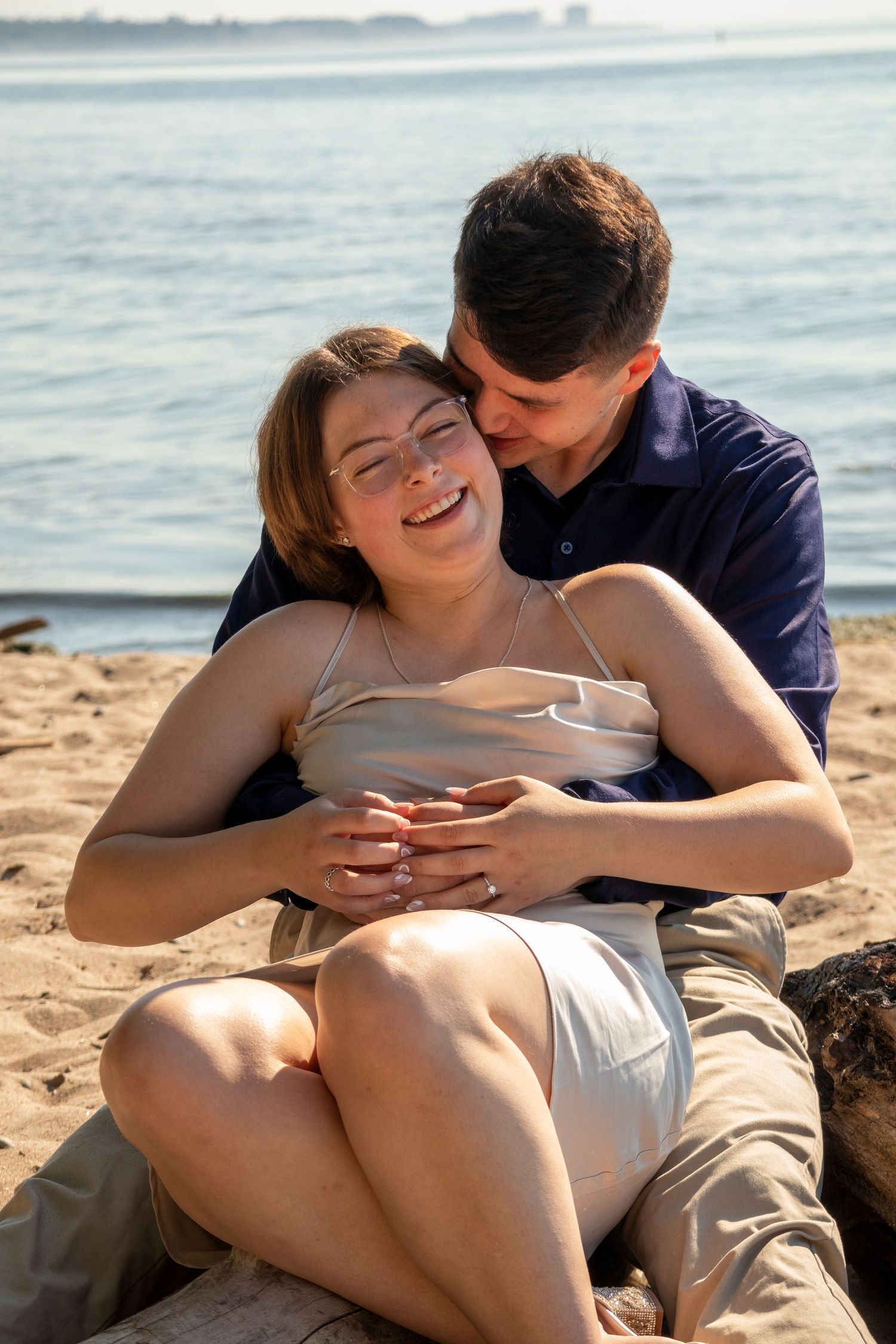 Engaged couple sitting on a beach hugging and laughing