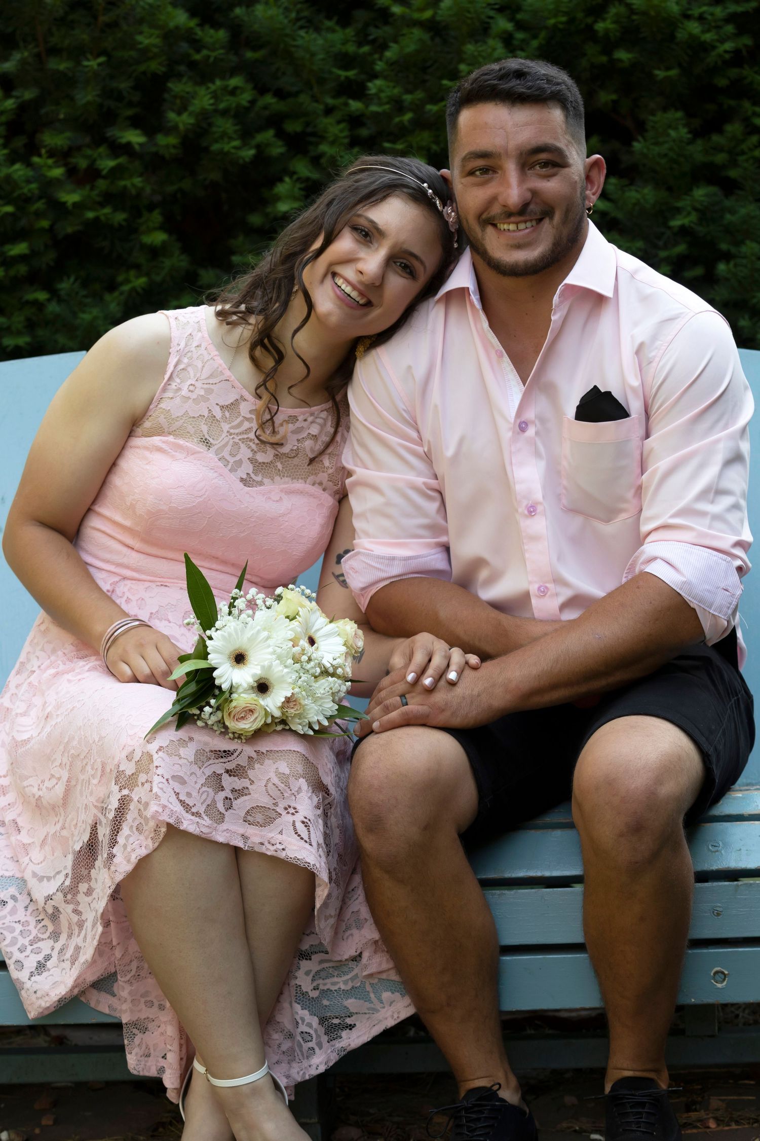 A bride in a pink dress leaning on the groom's shoulder.  Both are smiling