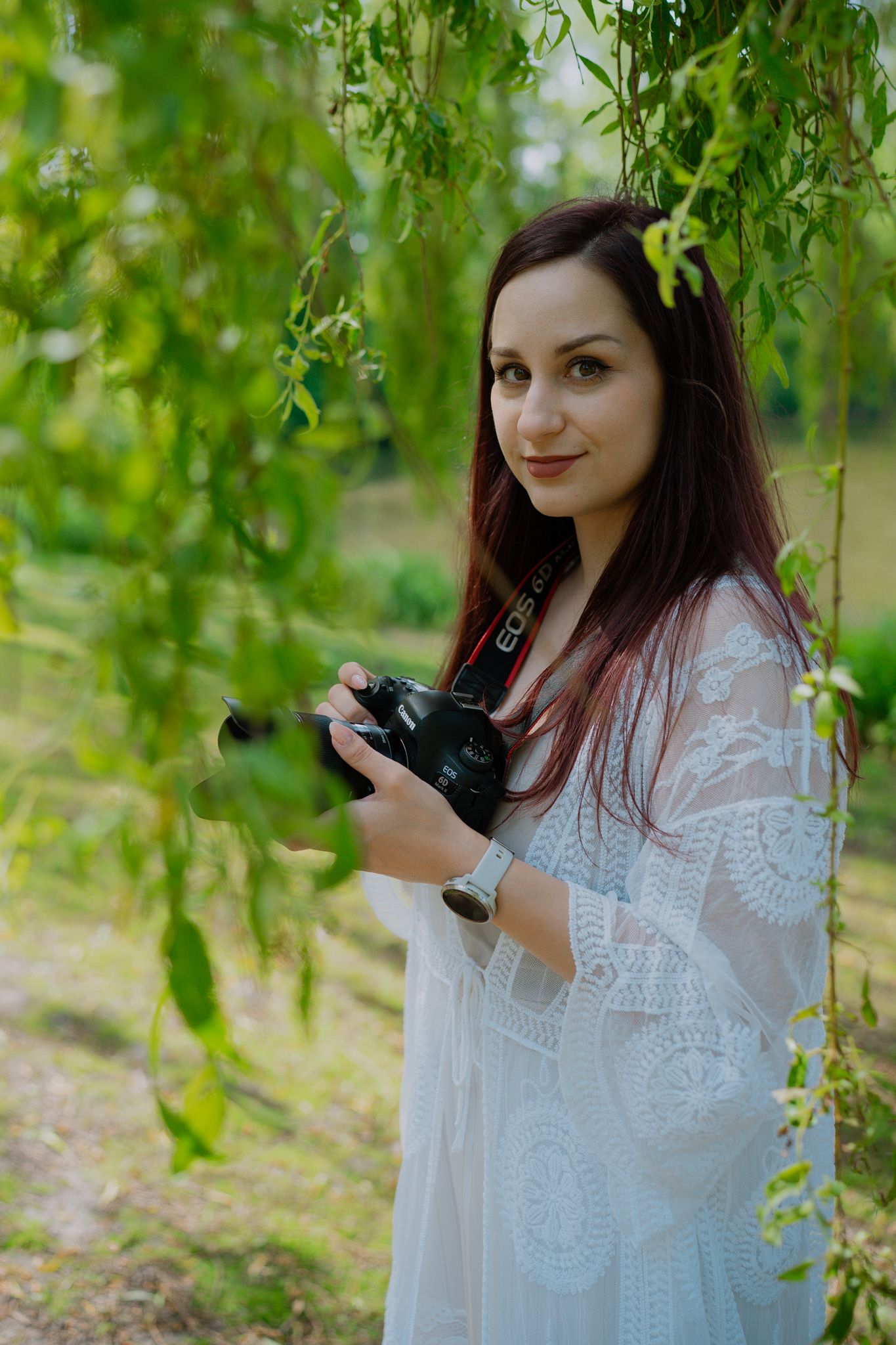 Photographer Boryana Mileva, founder of Avelim Photography, smiling for a photo with her camera between willow branches.