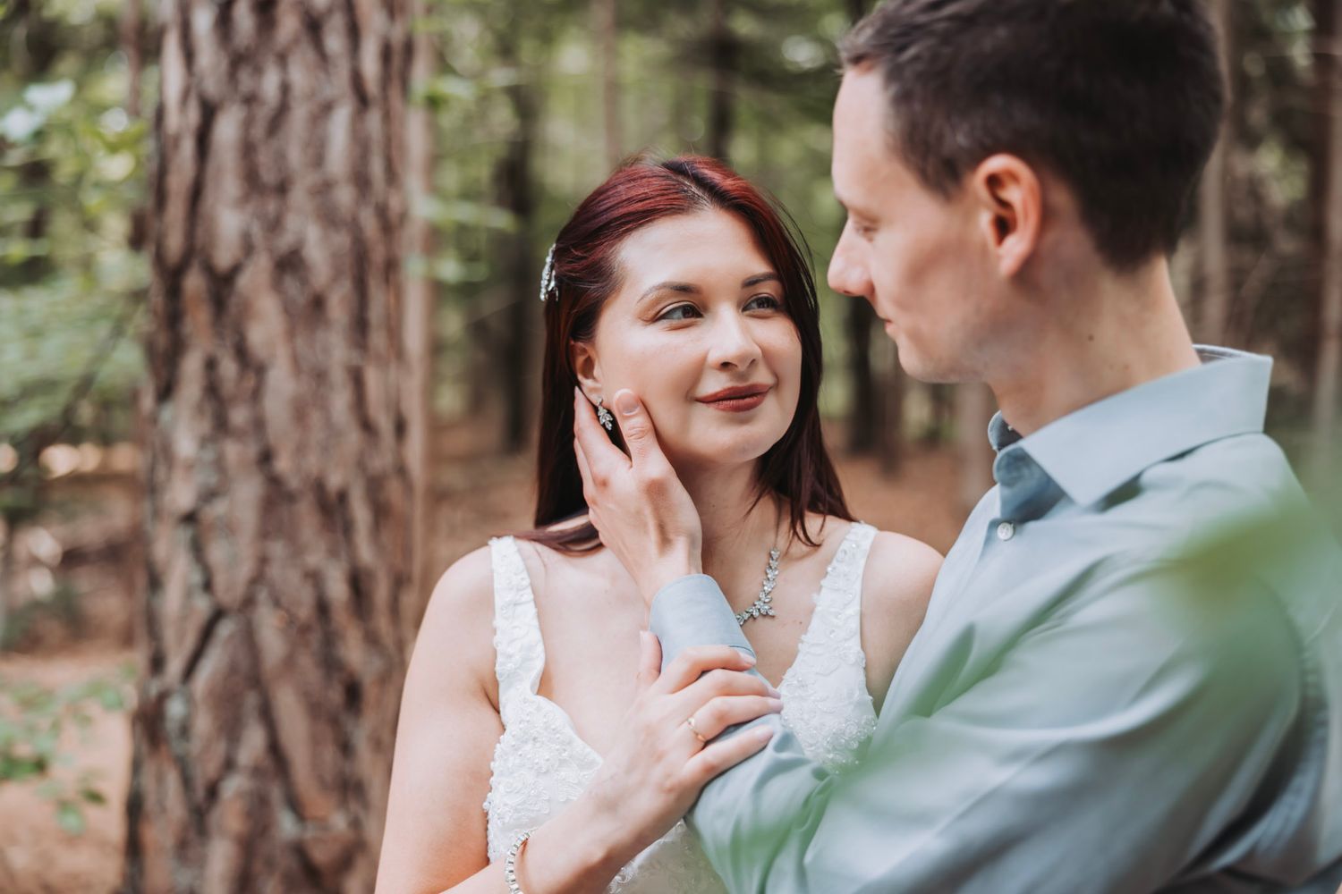 A couple shares tender moments together while standing among tall pine trees in a forest setting.