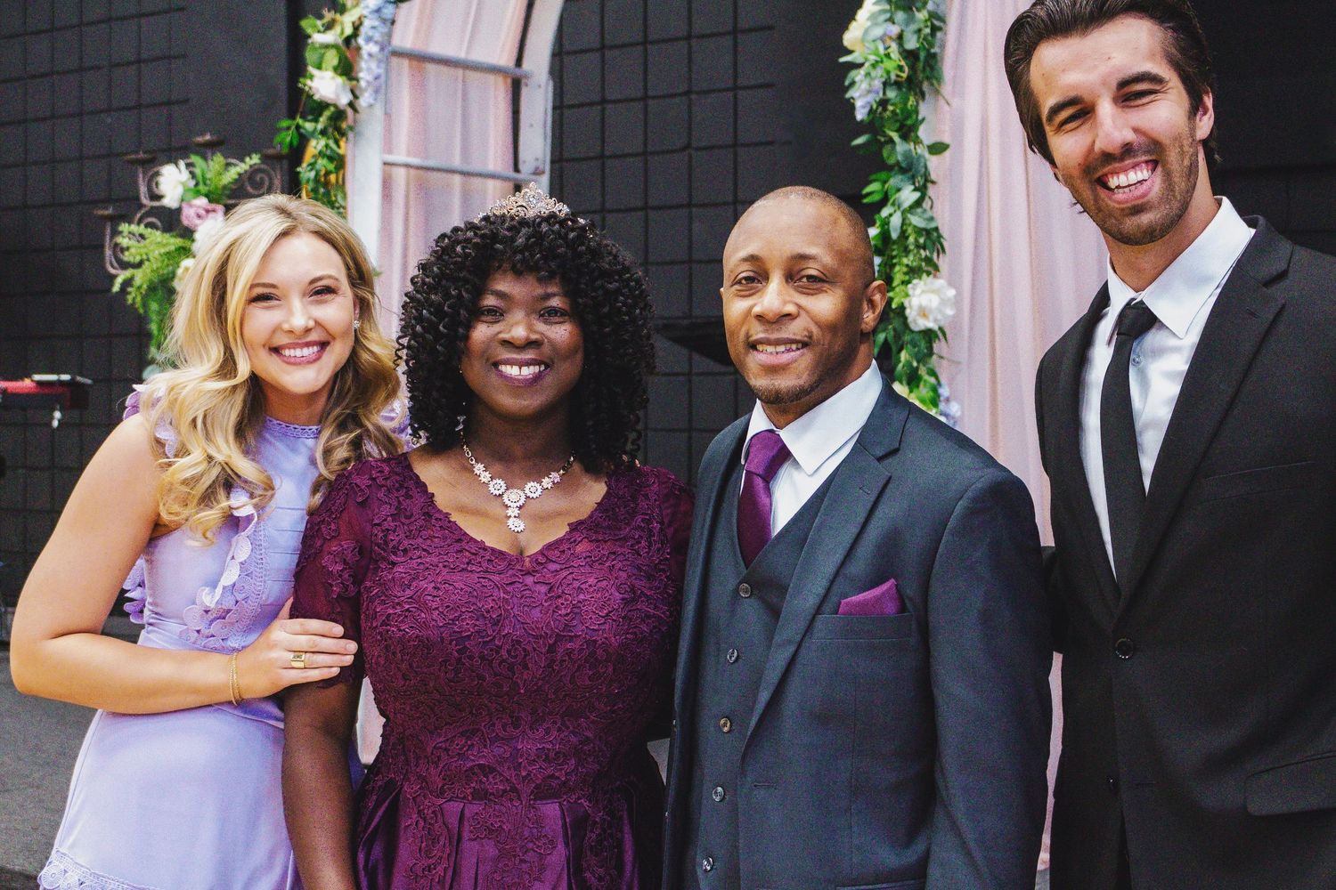 Four people dressed in formal attire including purple and black stand together smiling at a special event.