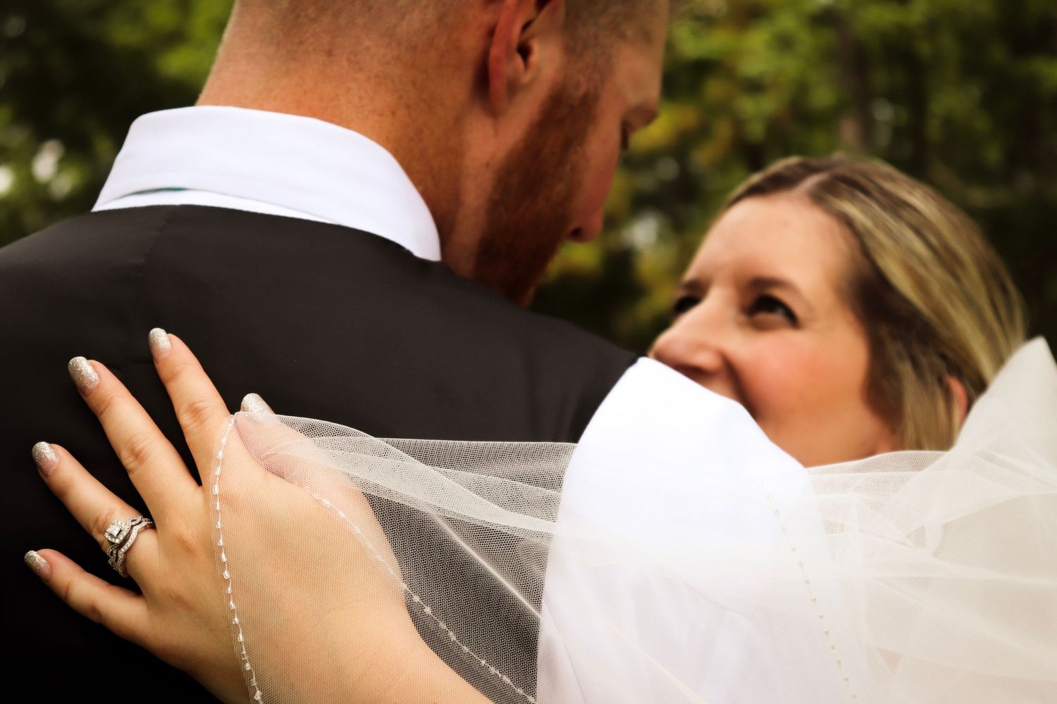 A romantic wedding couple shares an intimate kiss while the bride's veil flows in the breeze during their outdoor ceremony.