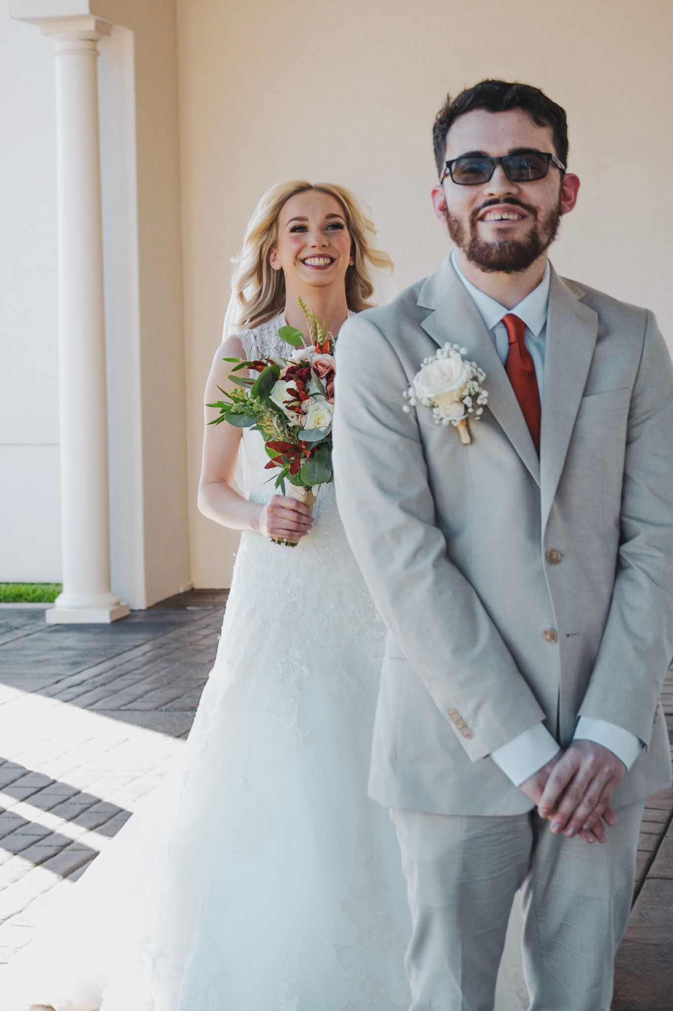 A couple in wedding attire shares joyful moments together in an elegant outdoor colonnade setting.