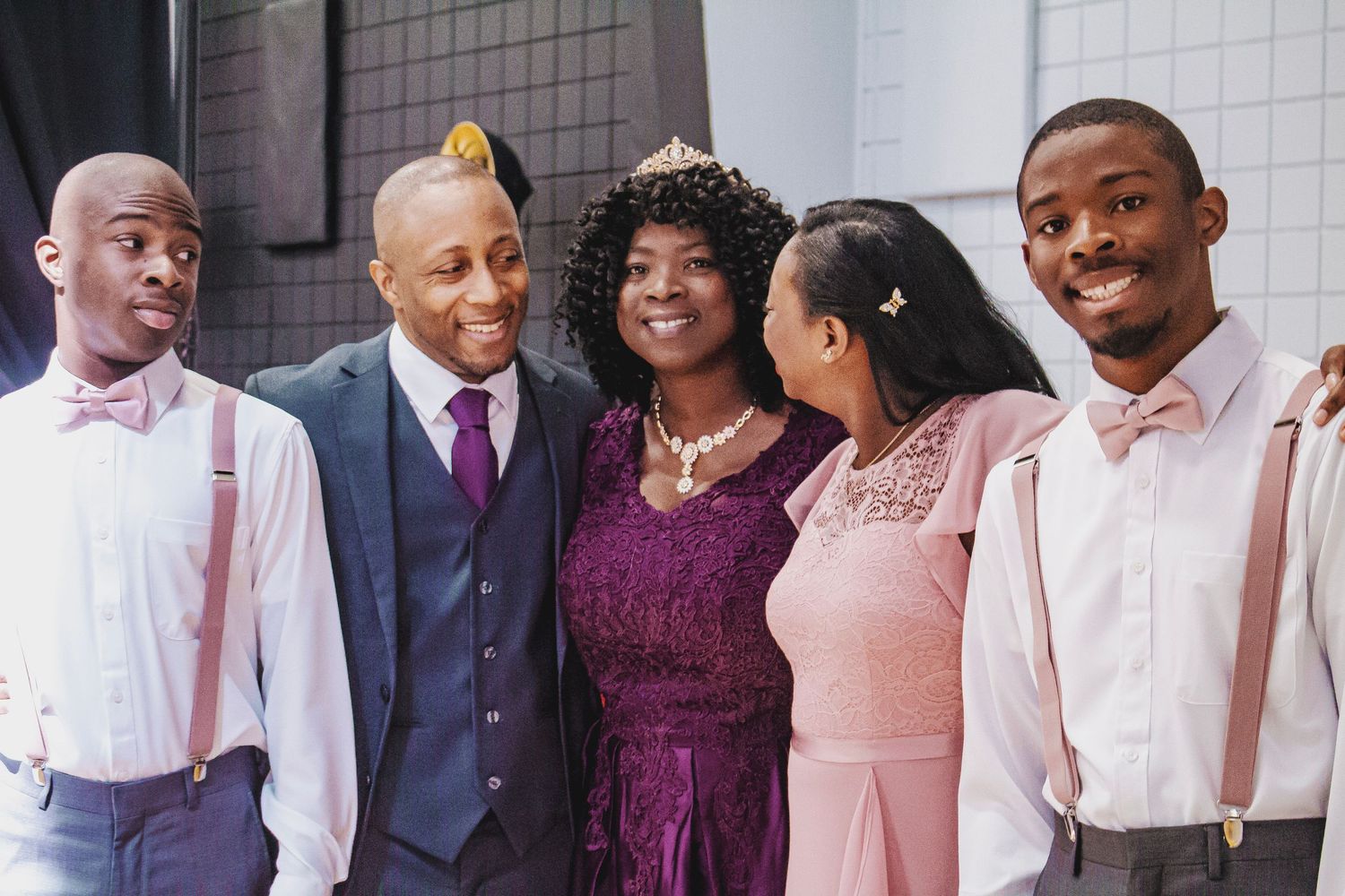 A group of wedding party members in formal attire including purple dresses and suits pose together for a photo.
