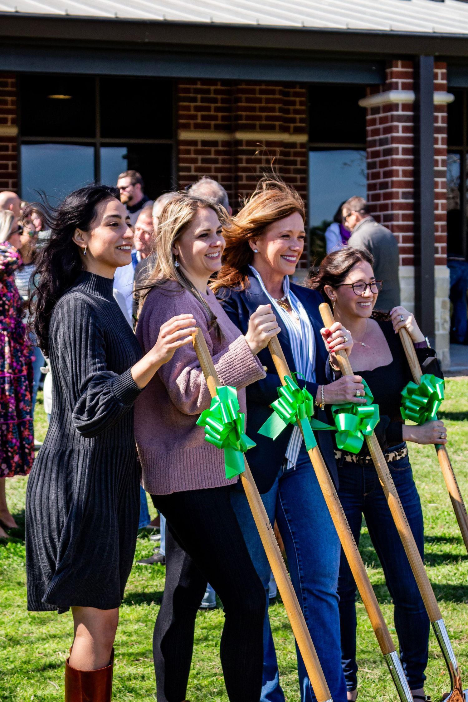 A group of people lined up outdoors holding ceremonial golden shovels with green ribbons during a groundbreaking ceremony.