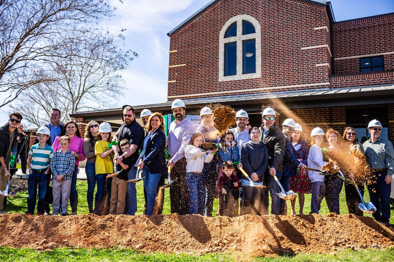 A large group of people stand in line against a brick building during an outdoor event.