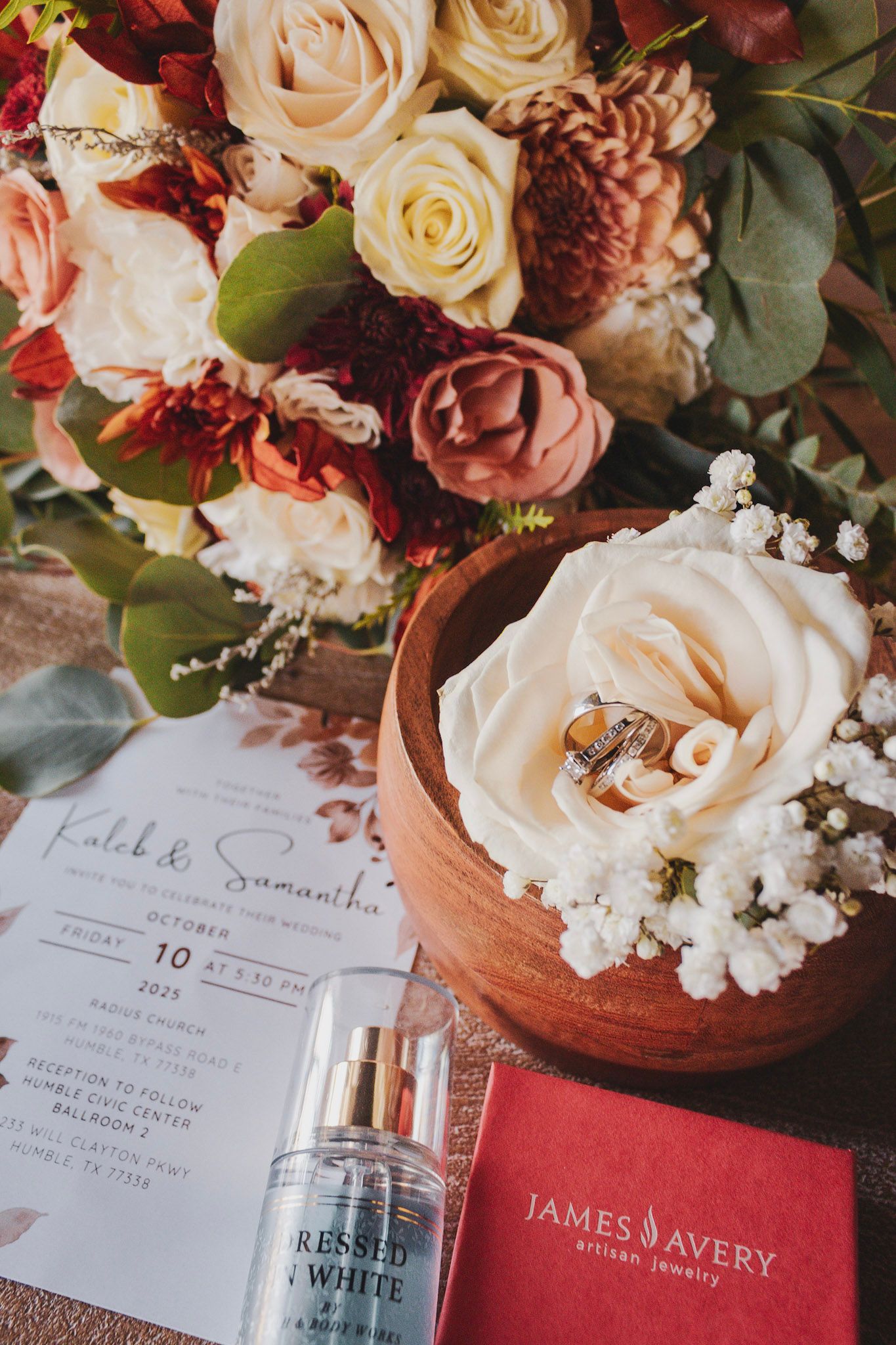 Wedding invitation suite with floral arrangements in cream and burgundy tones alongside perfume bottles and decorative details.