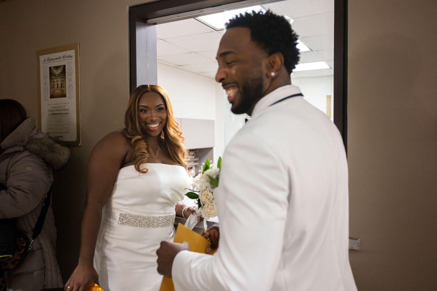 A couple stand at a reception window, smiling and laughing, while checking in for their city hall wedding (color version).
