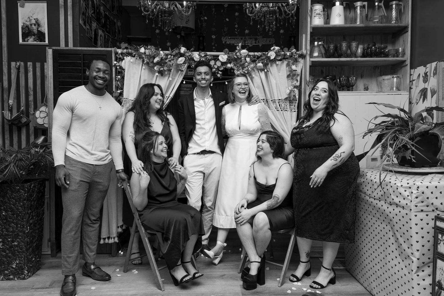 A candid picture of a group of friends with the bride and groom at a cafe micro-wedding. Two friends are seated, the couple in between (B&W)