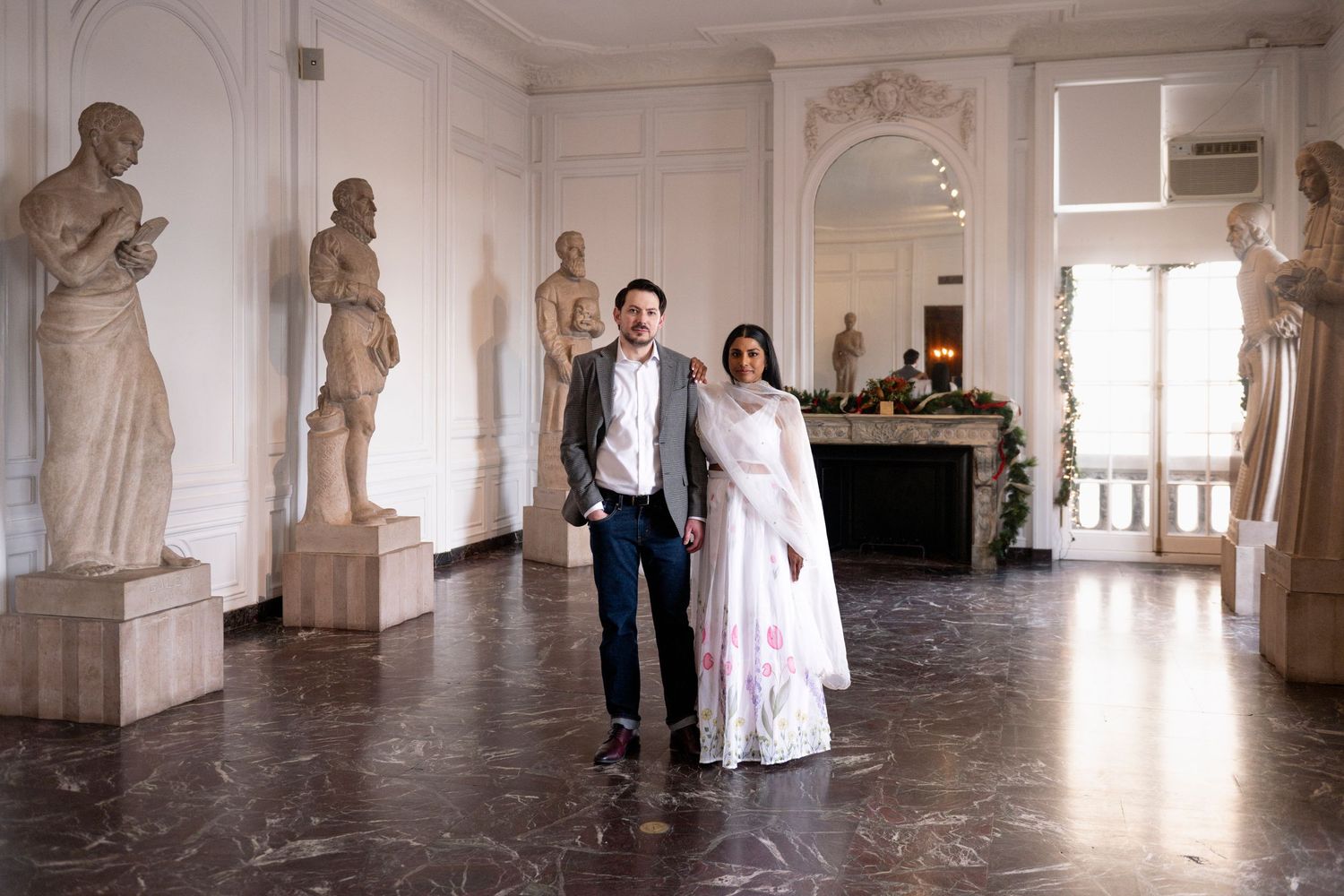A couple stand in the middle of a room of statues, facing the camera, inside Chicago's International Museum of Surgical Science.