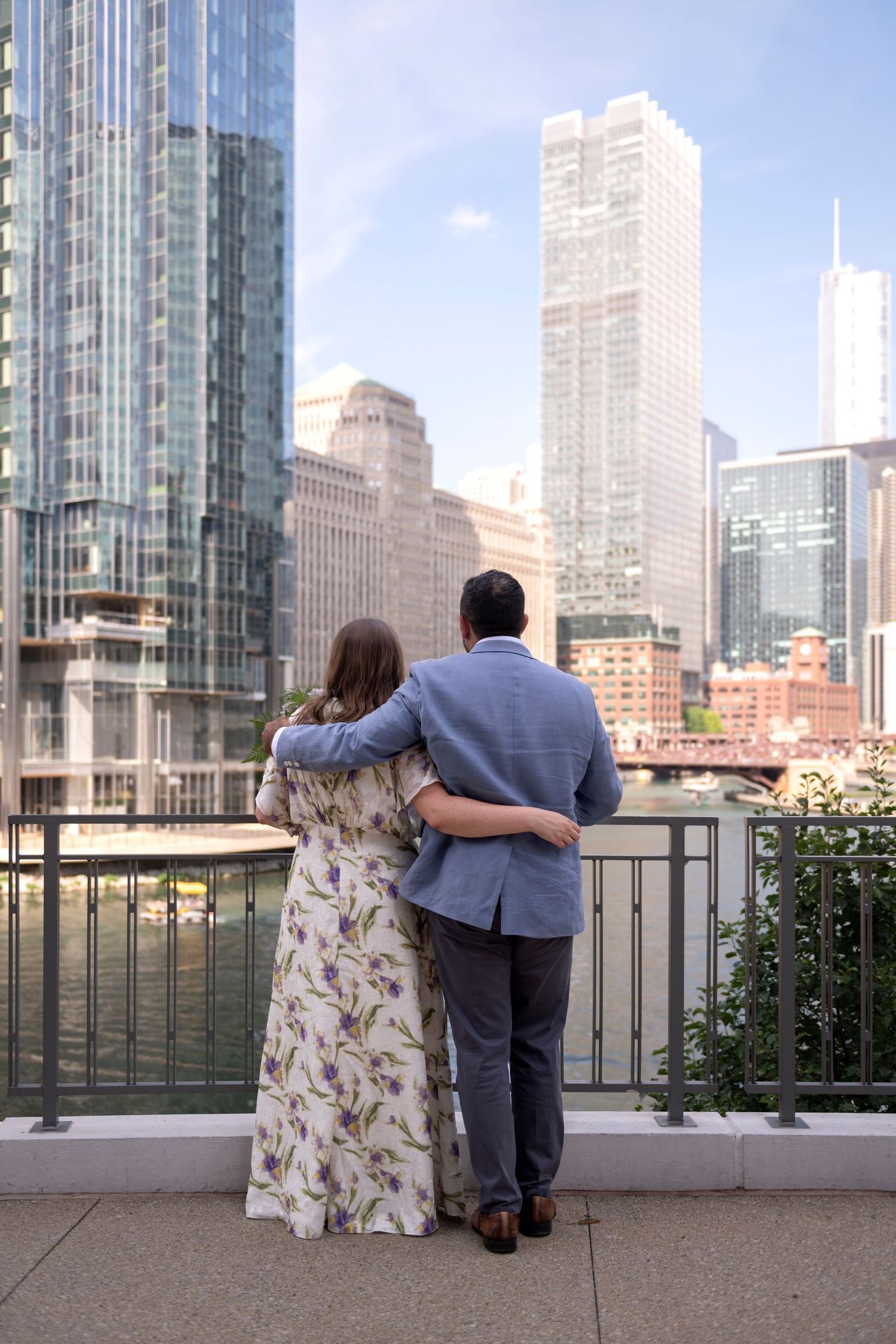 A newlywed couple stands overlooking the Chicago River with their arms around each other.