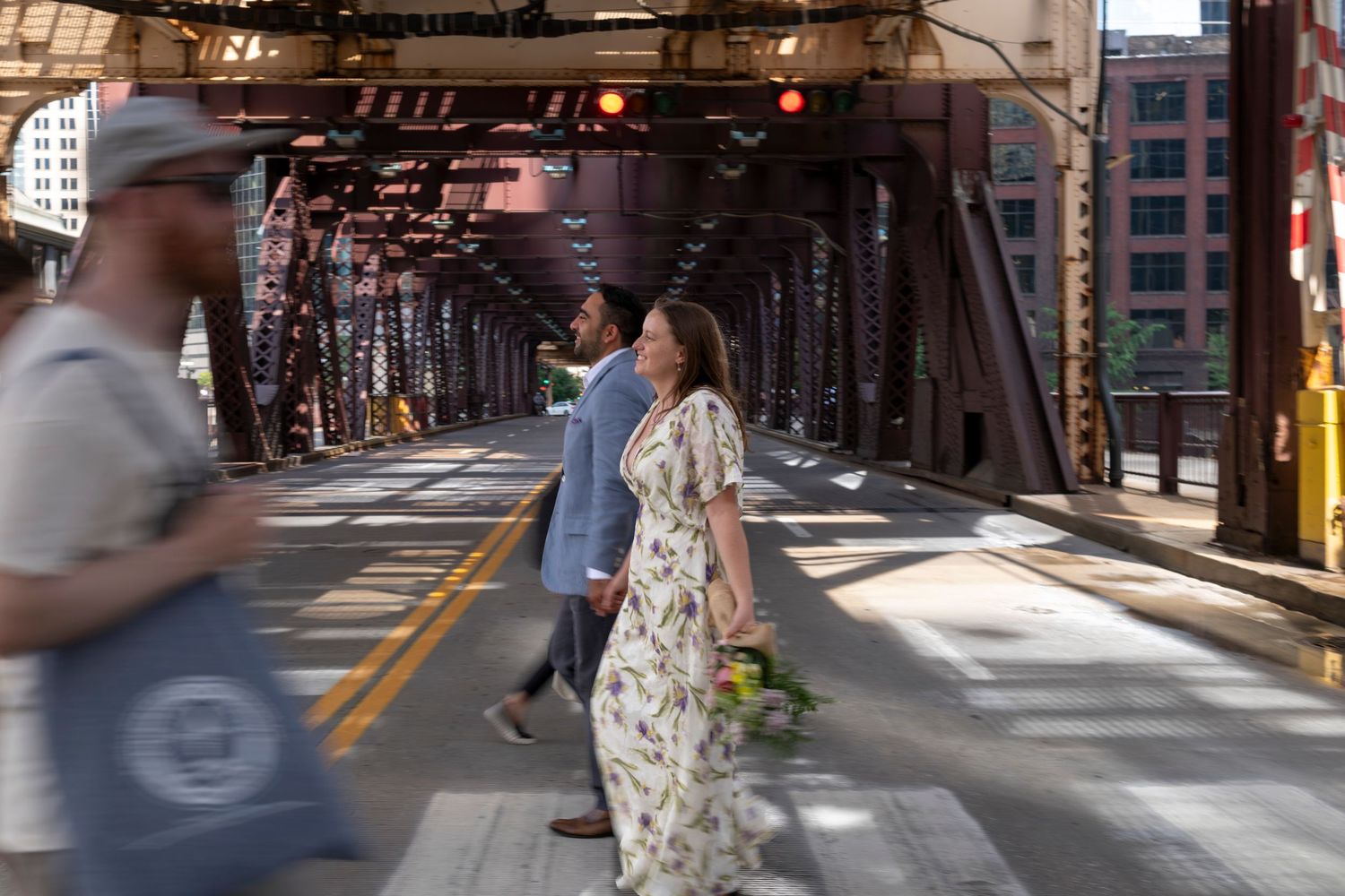 A newlywed couple walk across the street among pedestrians, with the elevated train tracks of Chicago's CTA in the background.