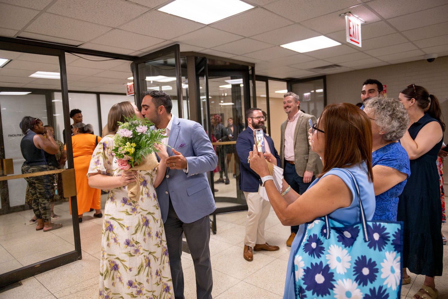 Family members take phone pics of a couple at City Hall, right after they signed their marriage license. The couple kisses for the photos.