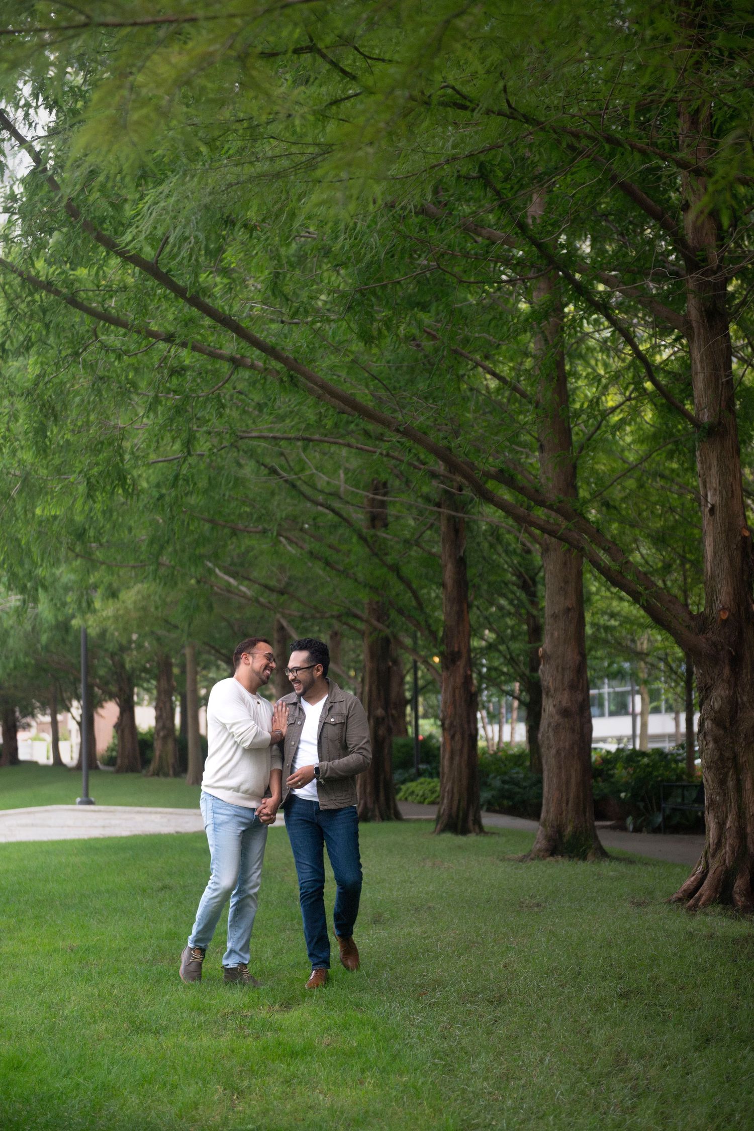 A gay couple lightly jostles each other while walking along a treeline in a Chicago park.