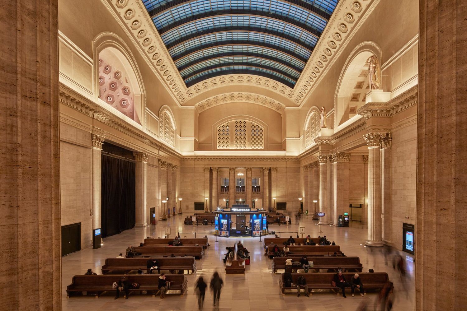 Travelers sit along bench pews and walk through the Great Hall at Chicago's Union Station, waiting for their trains.