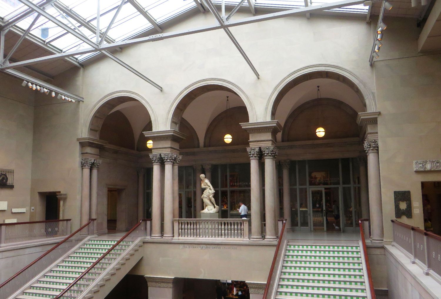 An empty Woman's Board Grand Staircase showing two of the stairways, three arches, and a statue in the center, lit by skylights.
