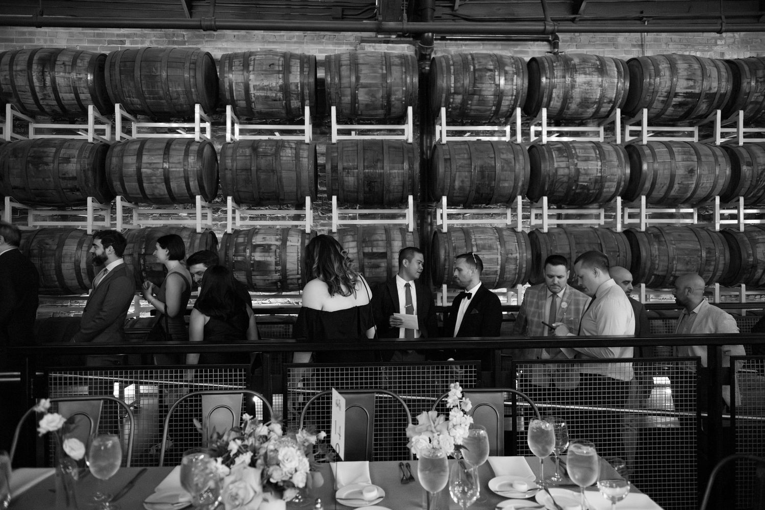 B&W - wedding guests arrive and mingle at the reception, in front of a wall of beer kegs at Goose Island Barrel House in Chicago.