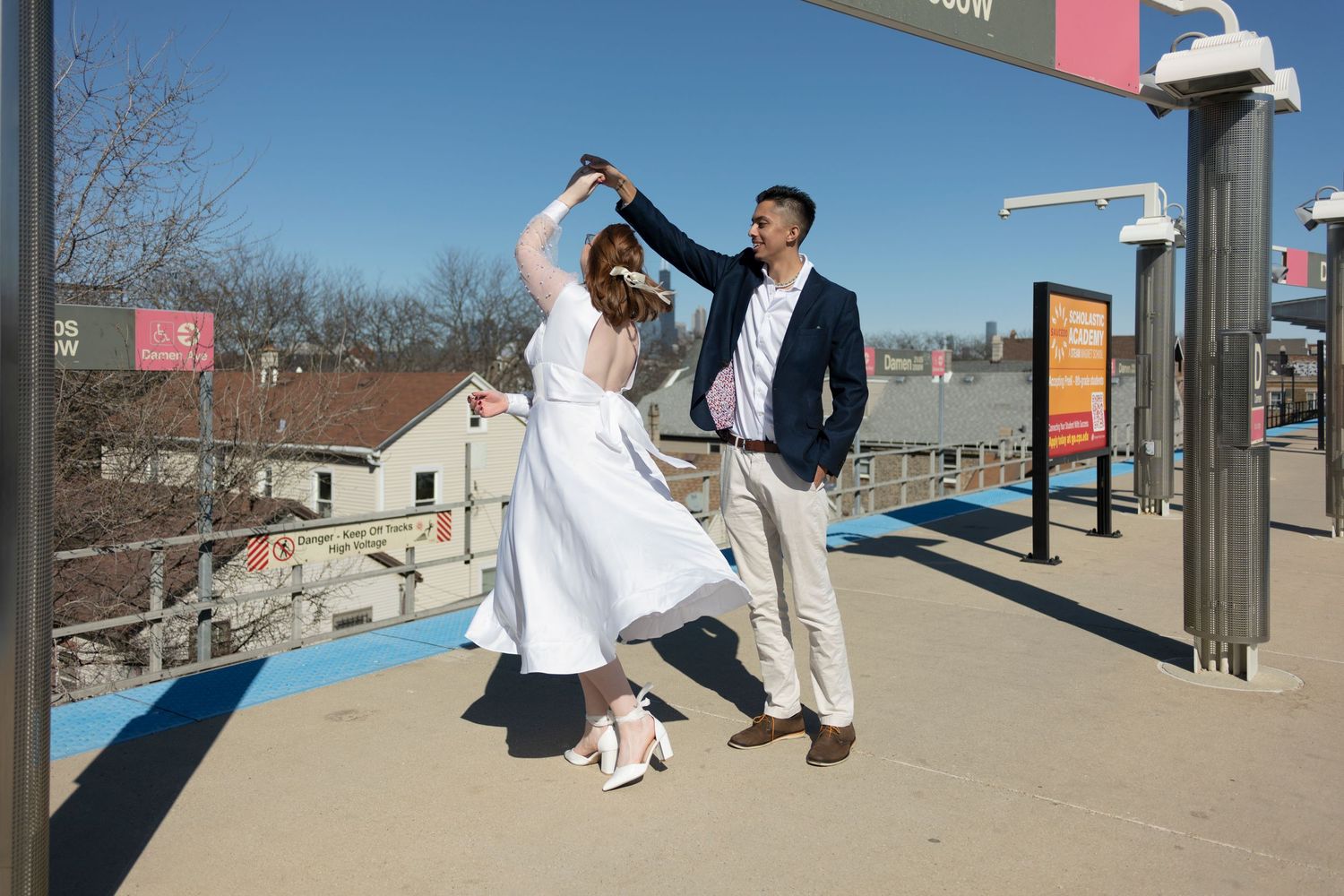 A groom twirls his bride on the train platform of the CTA in Chicago, with Sears Tower visible in between their figures.