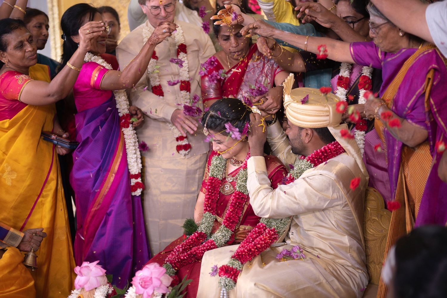 Standing loved ones throw flower petals over a seated newlywed couple at a South Indian (Tamil) wedding.