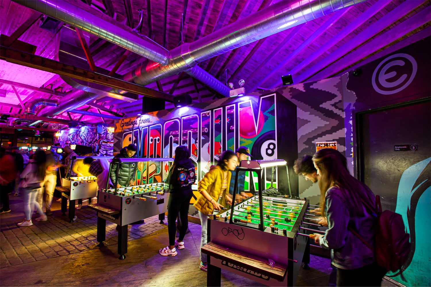 Patrons play arcade games in a neon-lit arcade bar.
