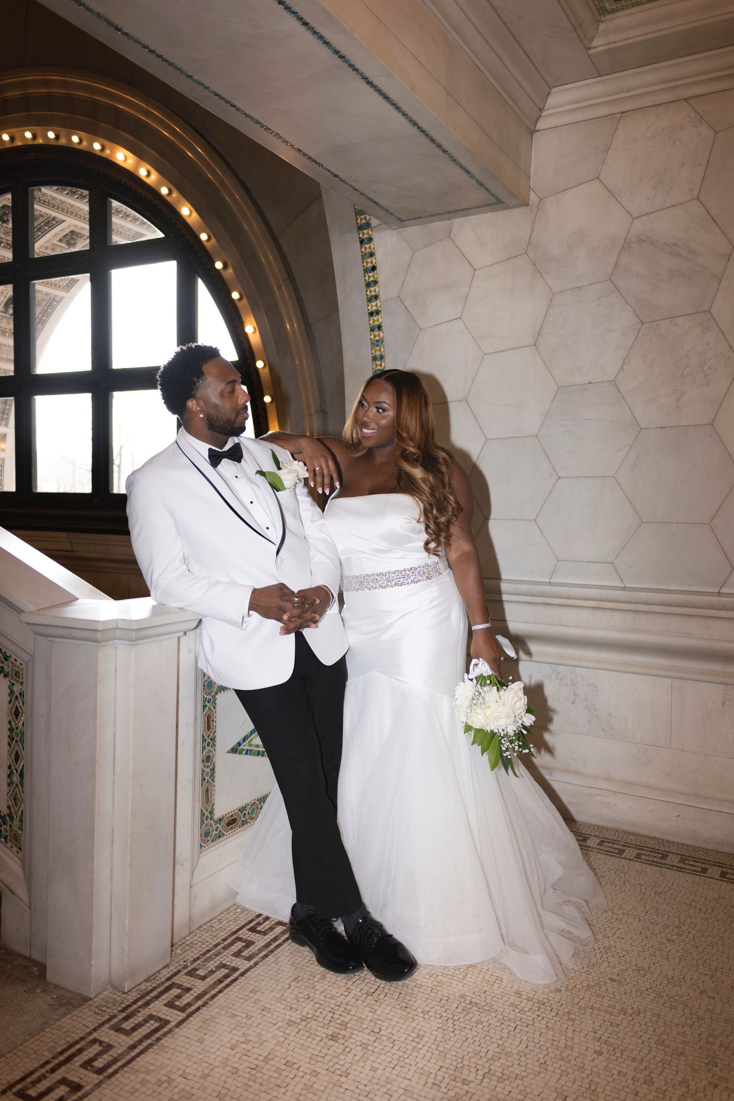A bride and groom lean to the side against a half wall inside the Chicago Cultural Center.