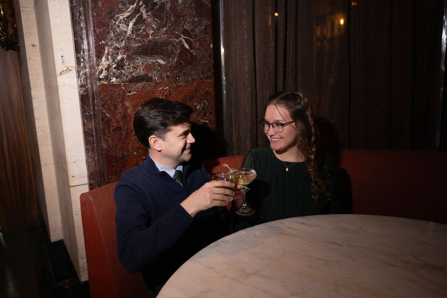 A couple clink cocktail glasses together while seated at a table at the Palmer House Hotel in Chicago.