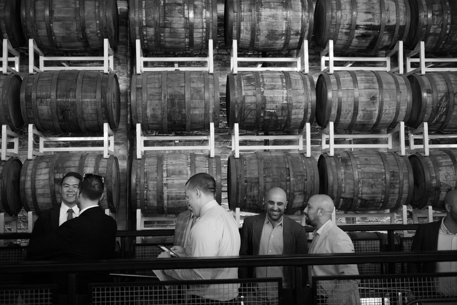 B&W - wedding guests arrive and mingle at the reception, in front of a wall of beer kegs at Goose Island Barrel House in Chicago.