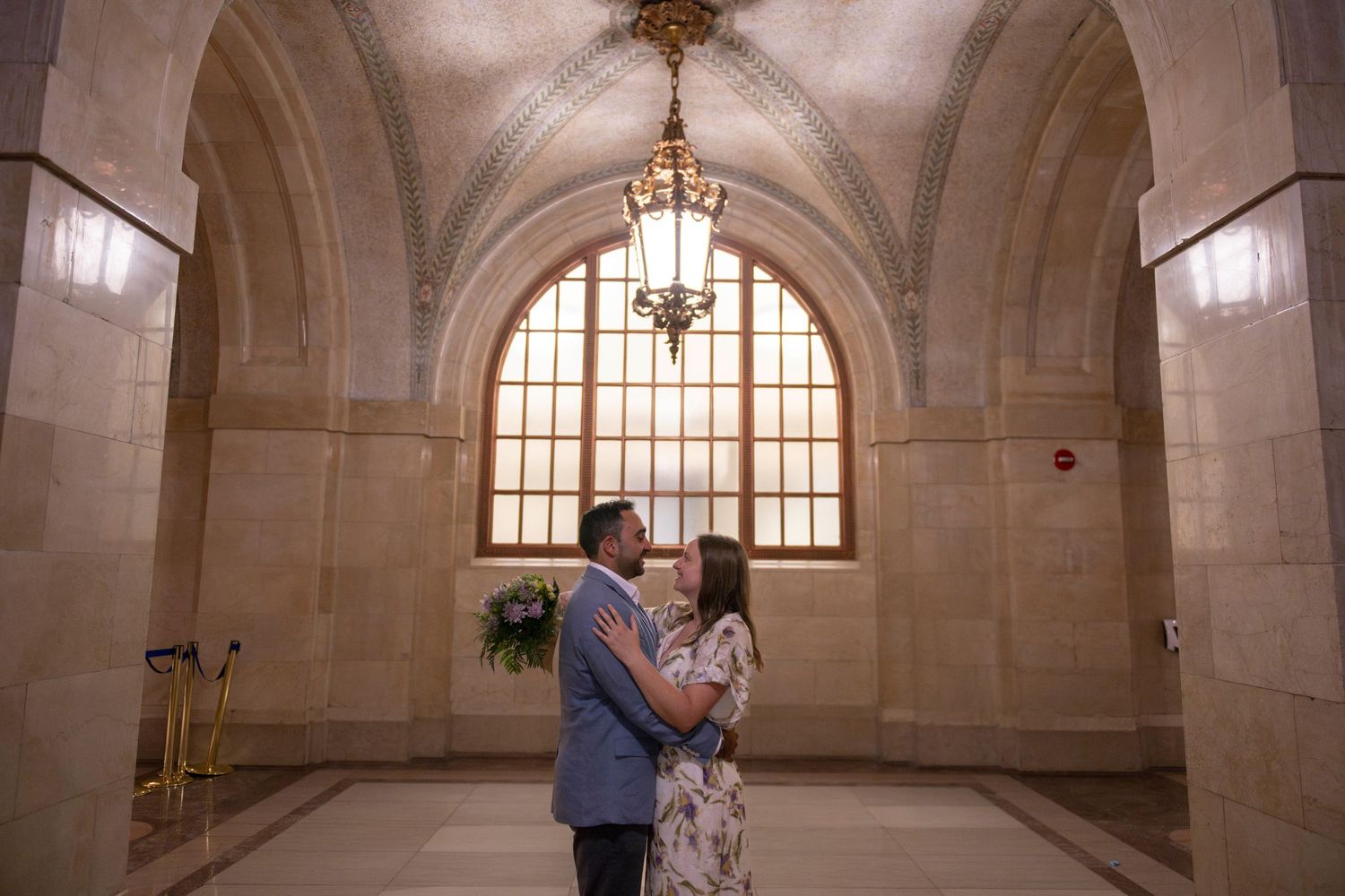 A couple face and embrace each other under archways and a chandelier inside Chicago's City Hall.