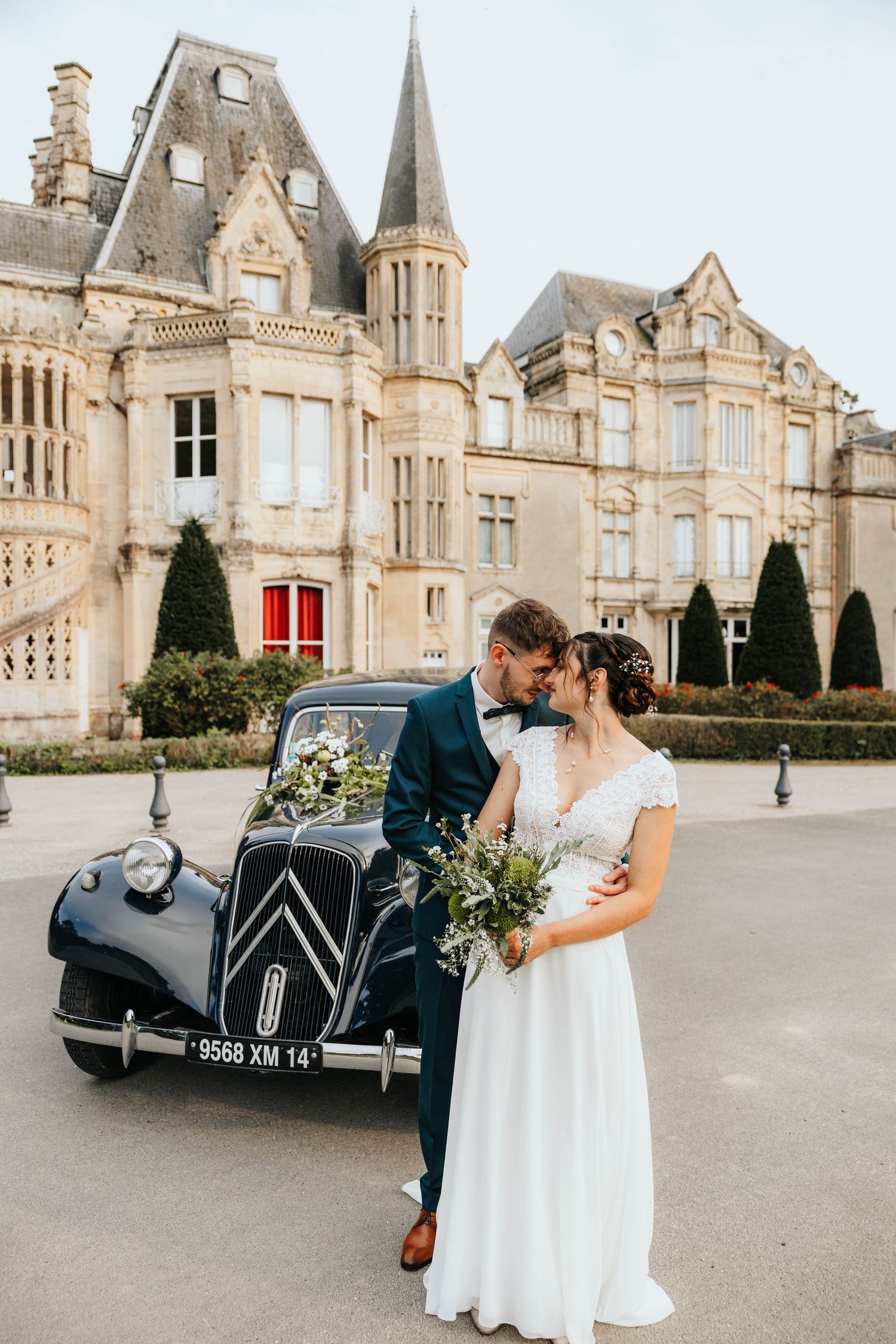 Bride and groom kissing beside a vintage Citroen car in front of a grand French chateau on their wedding day.