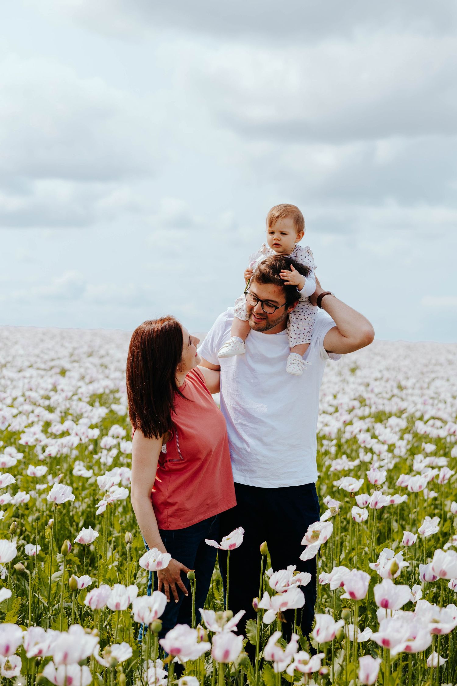 Happy family with baby on dad's shoulders smiling in a beautiful white poppy flower field.