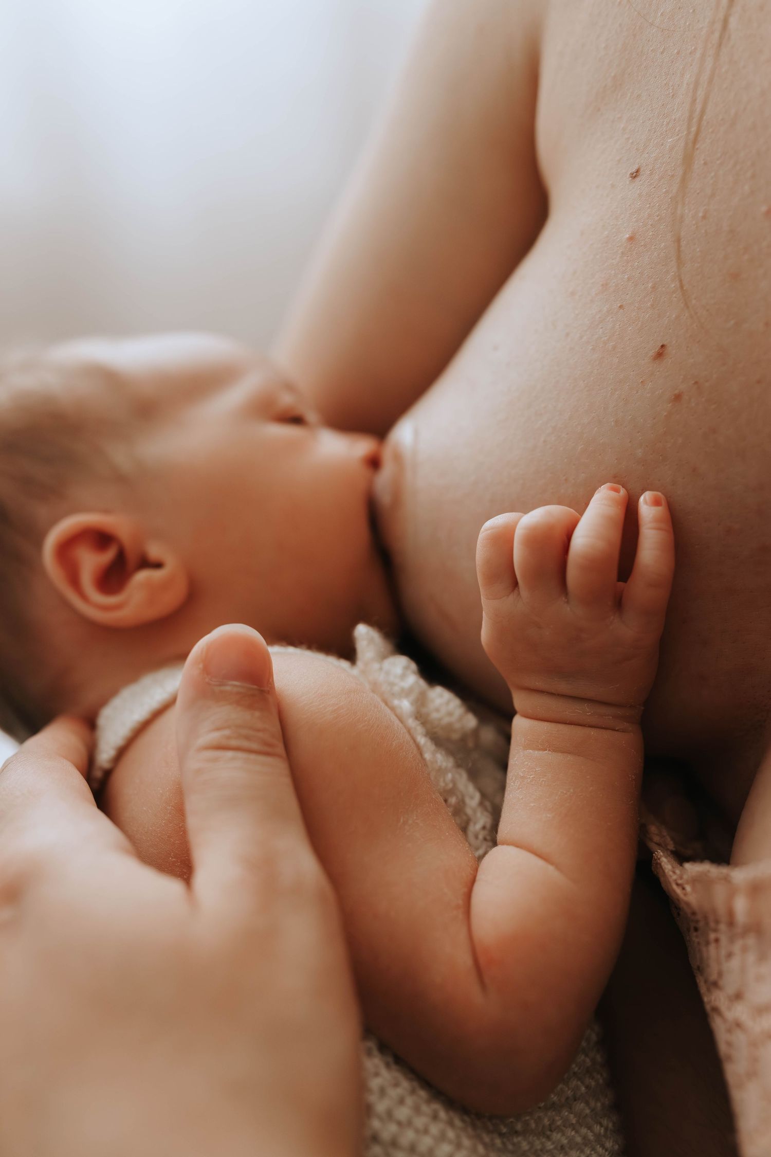 Close-up of mother breastfeeding newborn baby with tiny hand visible.