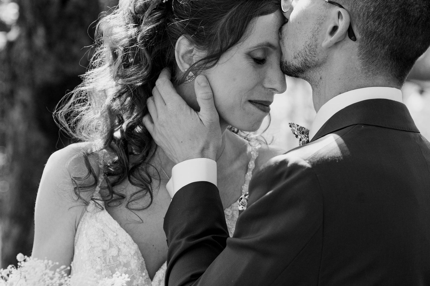Black and white wedding photo of groom tenderly kissing bride on forehead while cradling her face.