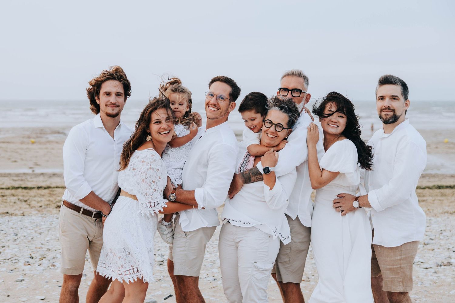 Happy multigenerational family in white outfits posing together on a cloudy beach.