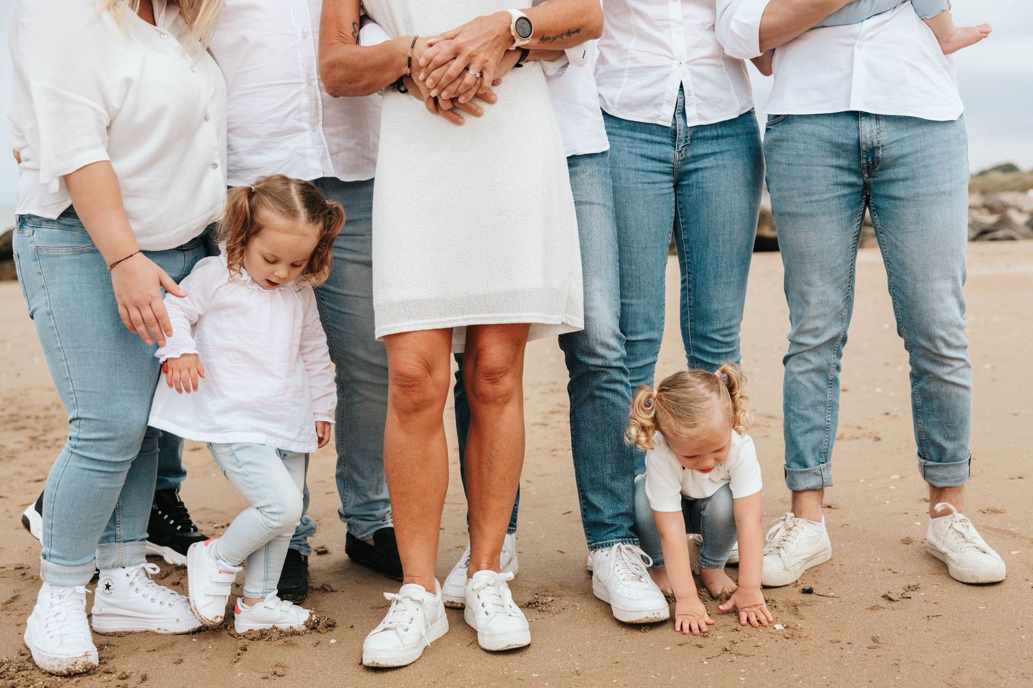 Family group photo on beach focusing on legs and two toddlers playing in sand.