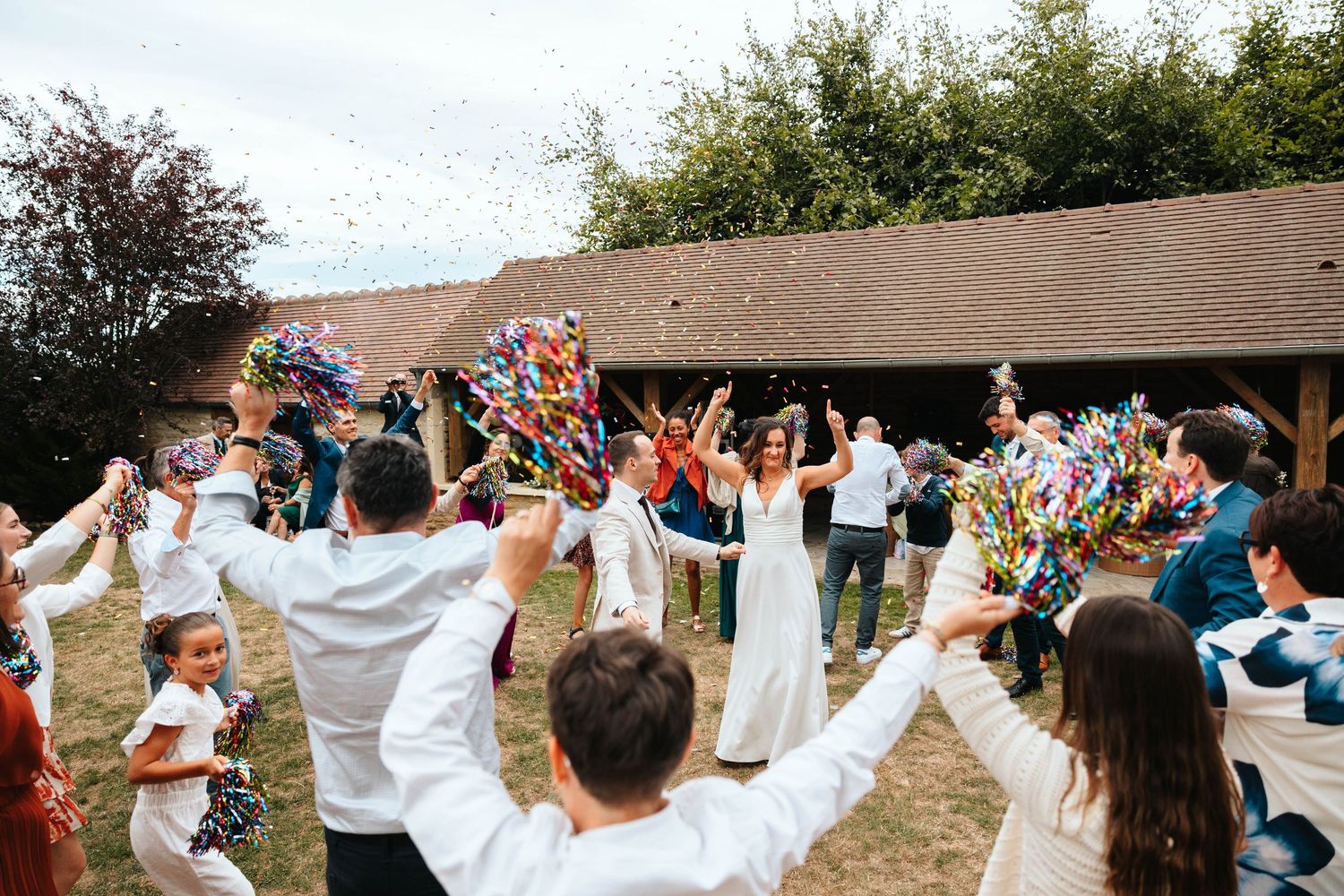 Bride surrounded by cheering wedding guests throwing colorful confetti streamers during joyful outdoor celebration.