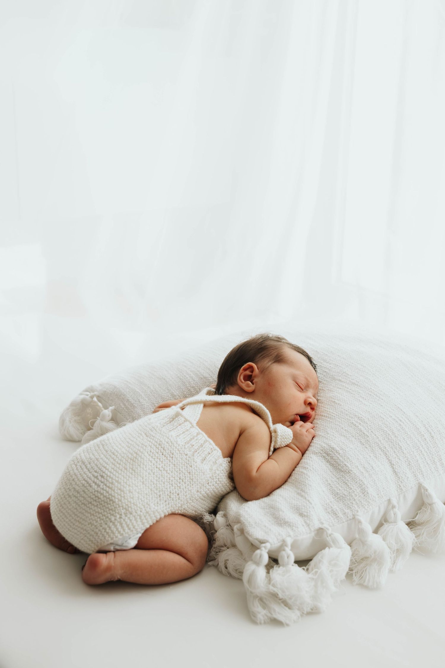 Sleeping newborn baby in white knit romper lying on soft white pillow.