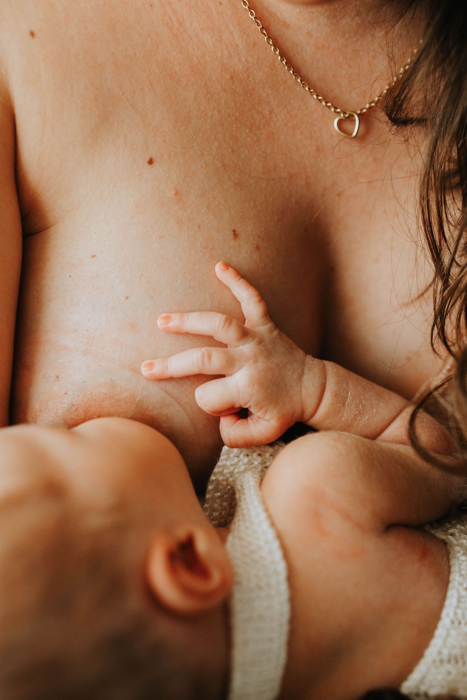 Close-up of mother breastfeeding newborn baby with small hand reaching up.